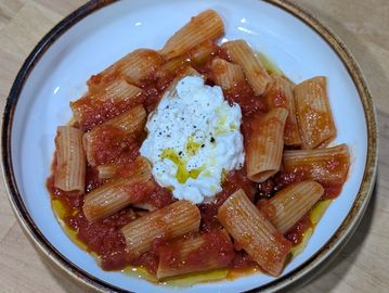 Plate of rigatoni pasta with tomato sauce and a dollop of ricotta cheese.