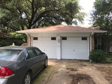 A car parked in front of a two-car garage under trees.