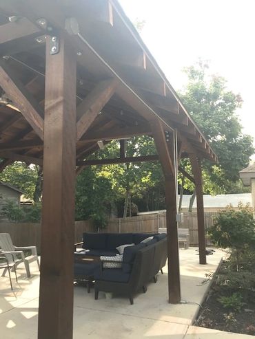 Wooden pergola with outdoor seating in a backyard.
