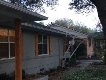 A gray house with wooden window shutters and a porch under trees.