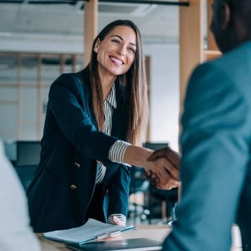 Businesswoman smiling and shaking hands in an office setting.
