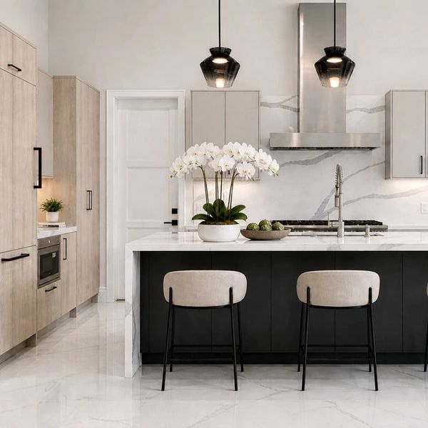 Modern kitchen with marble surfaces, black chairs, and pendant lights.