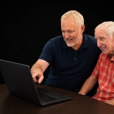 Two men smiling and looking at a laptop screen together.