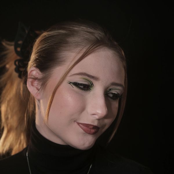 Young woman with creative green and black eye makeup against a dark background.