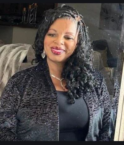 Smiling woman with braided and curly hair wearing a black outfit.
