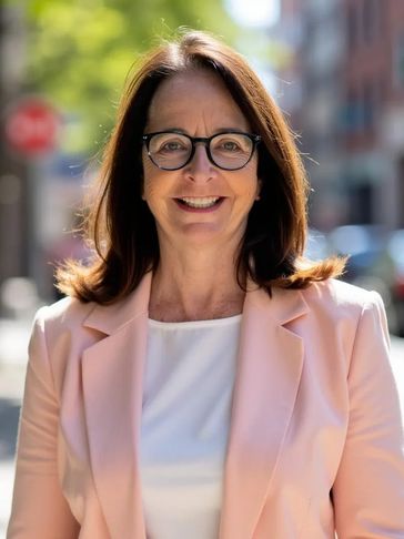 Smiling woman in glasses and pink blazer outdoors.