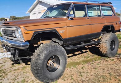 Vintage brown Jeep Wagoneer with large off-road tires and lifted suspension.