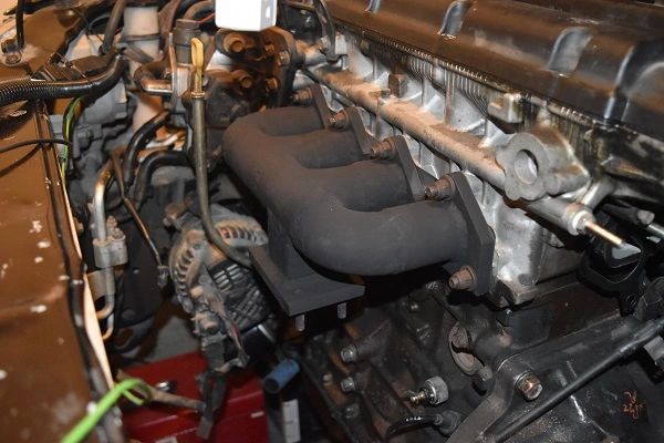 Close-up of a car engine with visible exhaust manifold and alternator.
