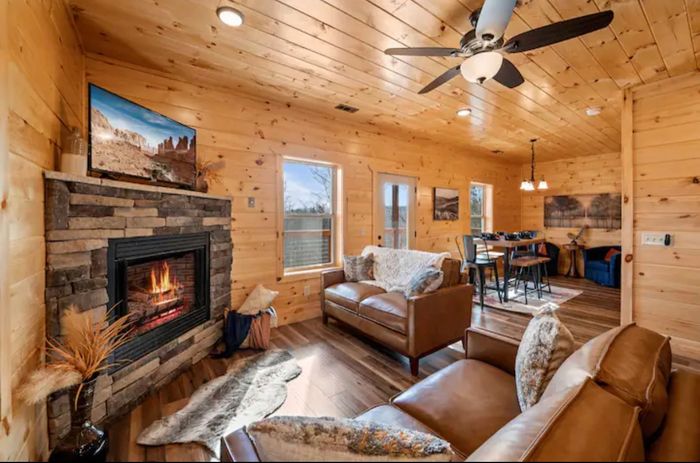 Beautifully furnished log cabin leather sofas facing a stone fireplace flat-screen TV on the mantel