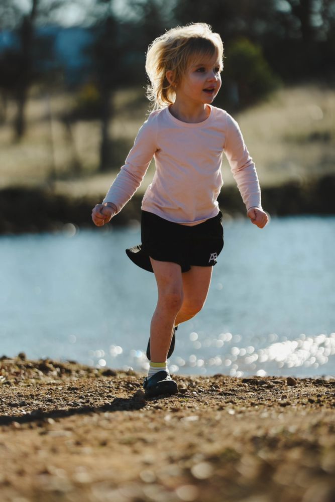 Young girl running joyfully by a lakeside on a sunny day.
