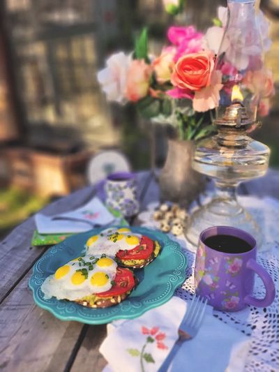 Rustic breakfast with fried eggs, tomato slices, coffee, and fresh flowers on a wooden table.