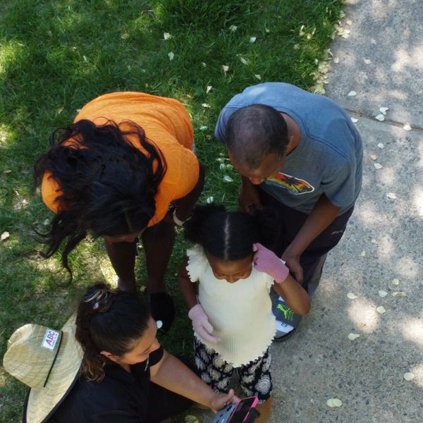 A family of four looking at a phone together outdoors on a sunny day.