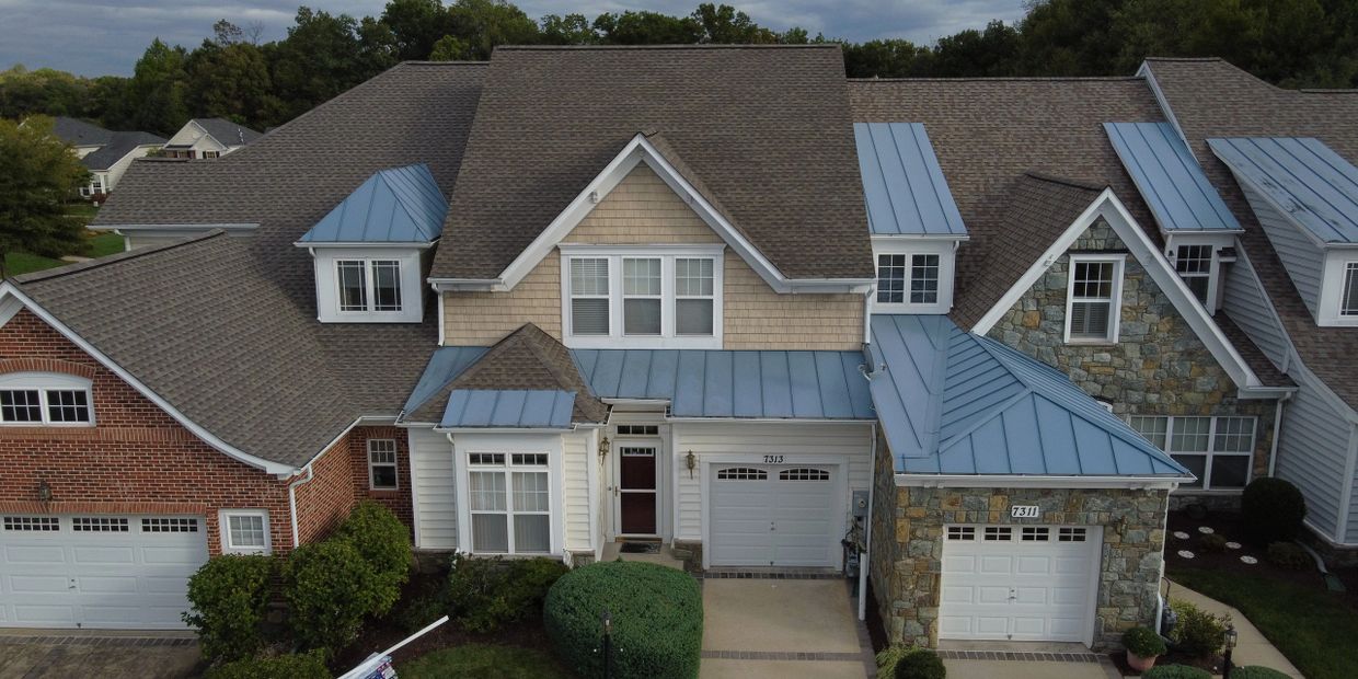 A large suburban house with mixed brick, siding, and stone exterior and blue metal roof accents.