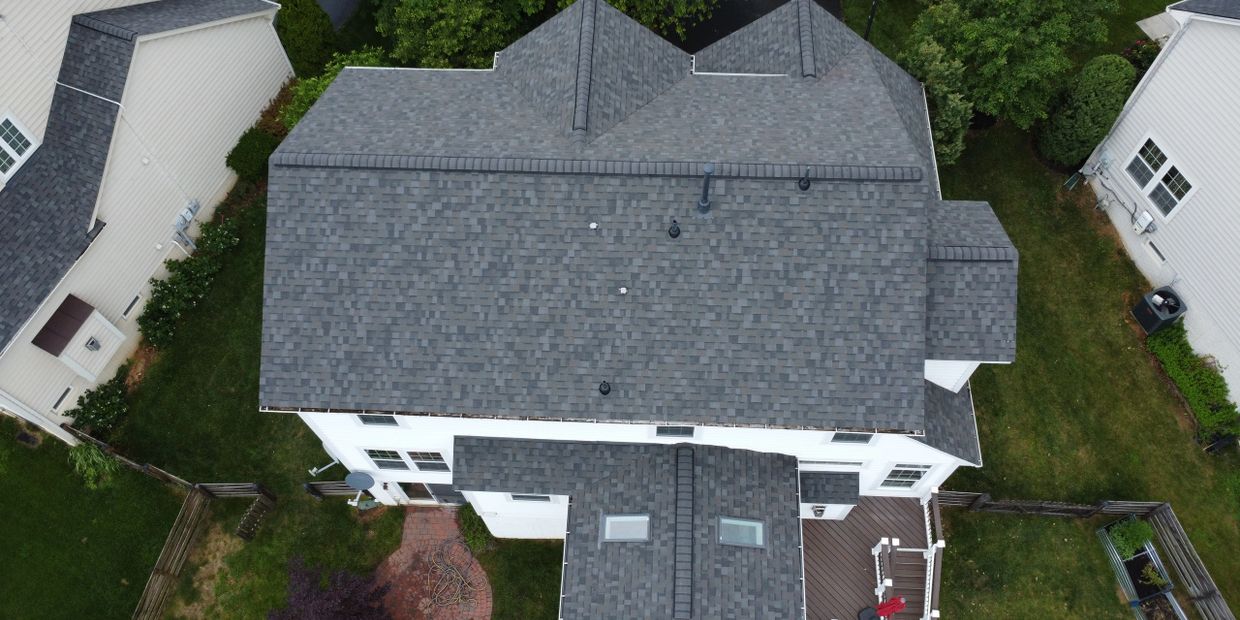 Aerial view of a white house with a gray shingled roof and surrounding green yards.