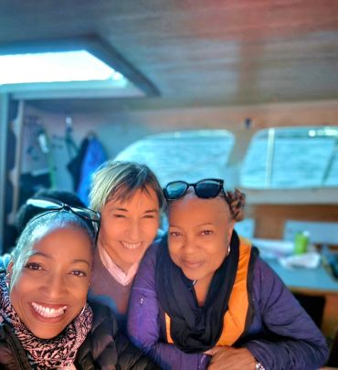 Three women smiling together inside a boat with ocean views.