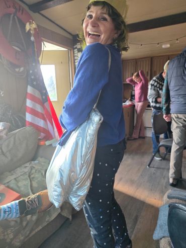 Woman smiling indoors with a silver bag and American flag in background.