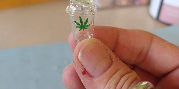 Hand holding a tiny clear plastic cup with green leaf designs.
