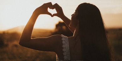 Girl making a heart with her fingers at sunset