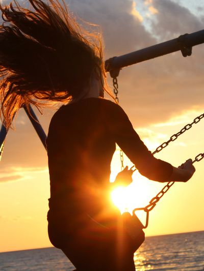 Girl on a swing by the ocean at sunset