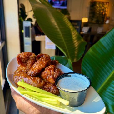Plate of saucy chicken wings with celery and ranch dressing.