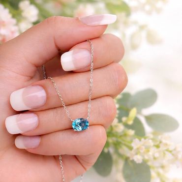 Hand holding a silver necklace with a blue gemstone pendant.