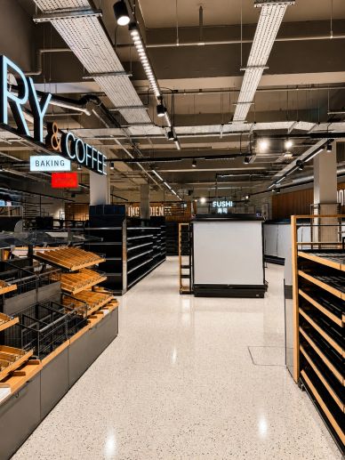 Empty shelves in a modern grocery store with signs for bakery, coffee, and sushi.