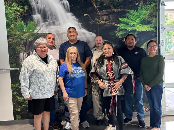 Group photo of eight people standing indoors with a waterfall mural.