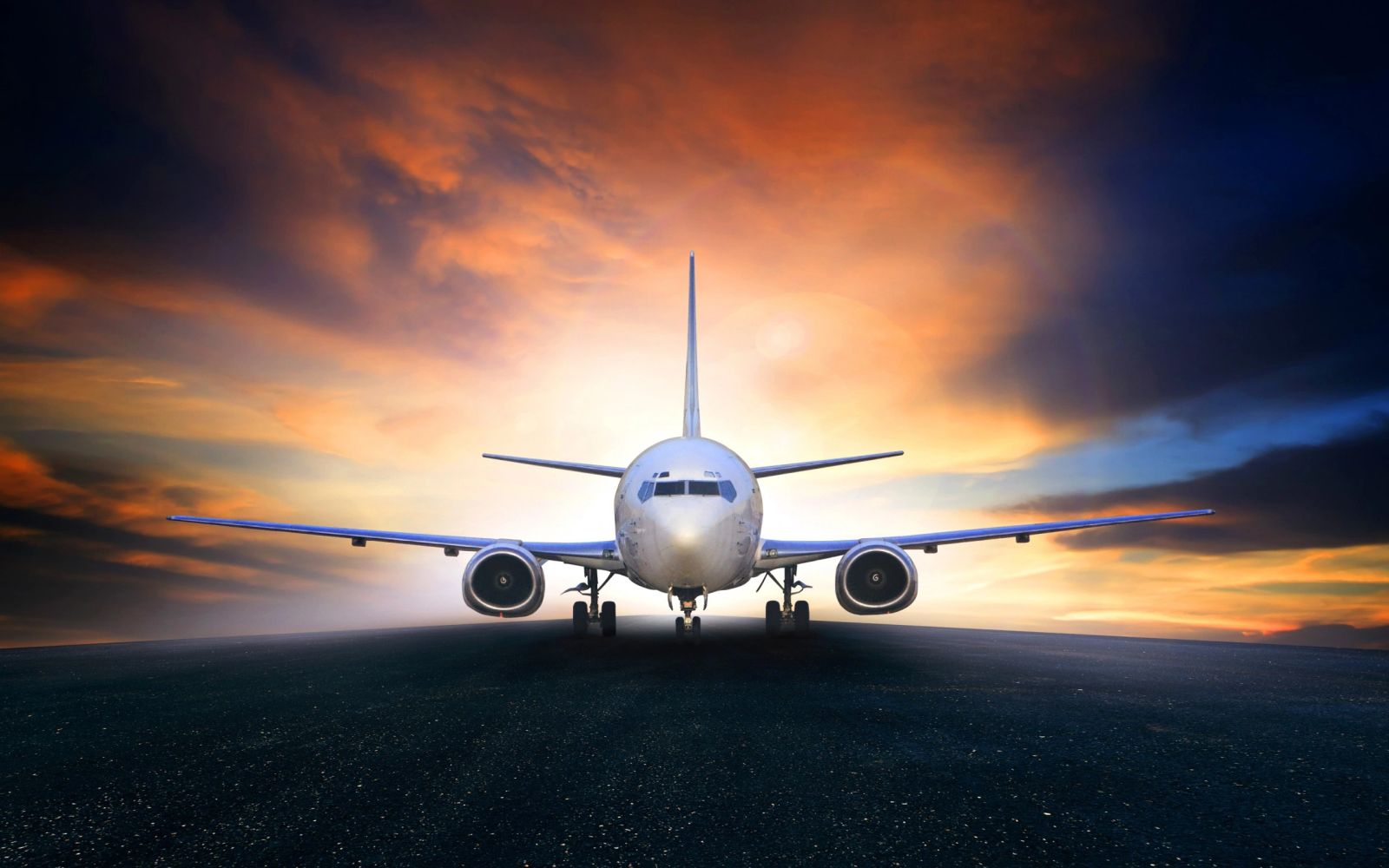 Airplane on runway with dramatic sunset sky in the background.