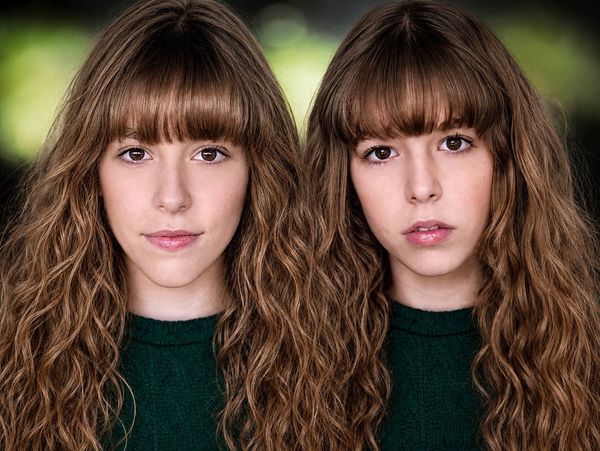 Identical twin women with brown curly hair and green sweaters.