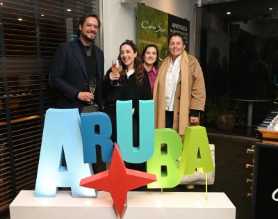 Cuatro personas posan detrás de un letrero luminoso de Aruba.