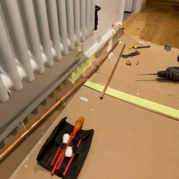 Radiator installation in progress with exposed copper pipework and professional tools