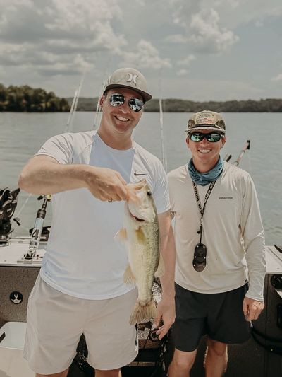 Two men on a boat proudly holding a freshly caught fish.