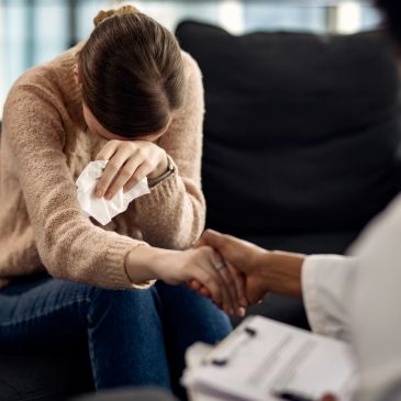 A woman crying and being comforted by a healthcare professional holding her hand.
