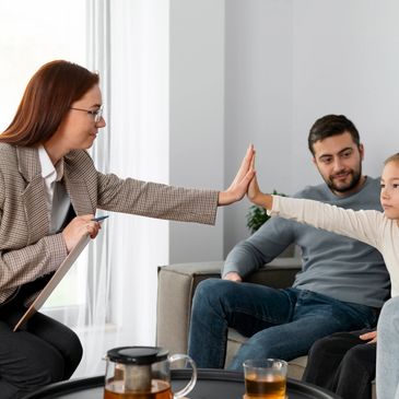Child giving a high-five to a woman during a family therapy session.