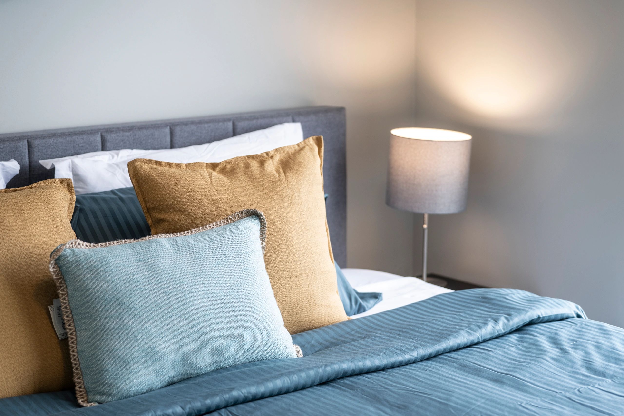 Comfortable bed with blue and tan pillows and a lamp.