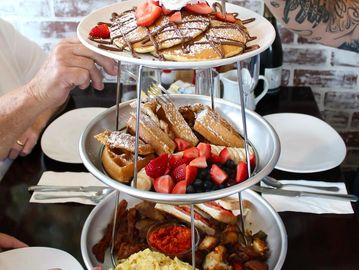 Three-tiered breakfast platter with pancakes, pastries, and savory dishes.