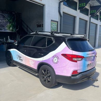 A black and pastel-colored SUV with business branding is parked outside a commercial building.