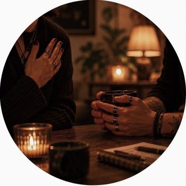 Two people with rings holding drinks in a cozy, candlelit setting.