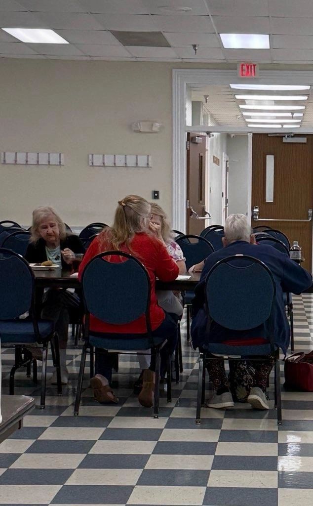 Elderly people sitting and eating together in a community room.