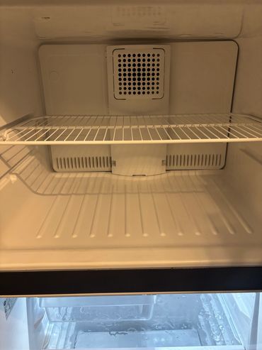 Empty refrigerator interior with a wire shelf and ventilation.