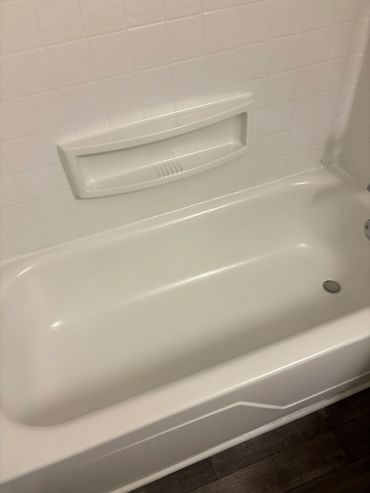 Clean white bathtub with built-in soap holder and tiled wall.