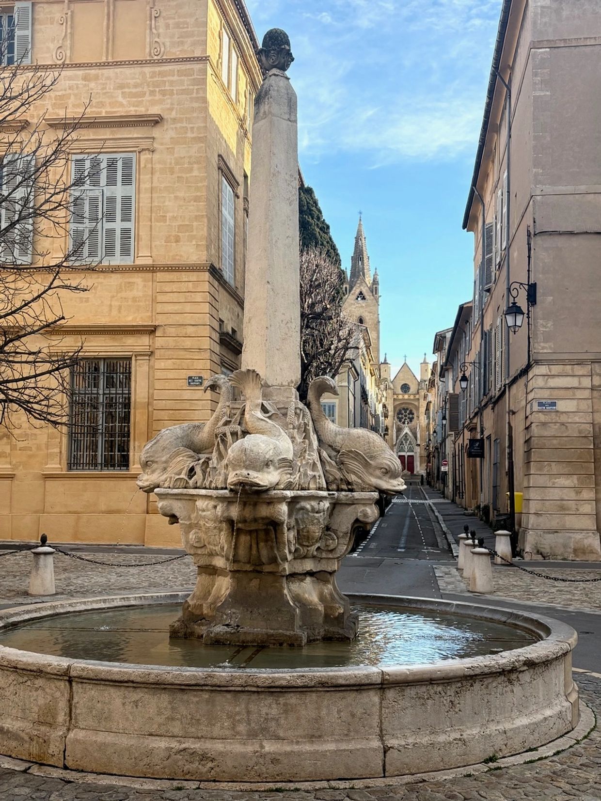 Historic stone fountain with fish sculptures in a quaint European street.