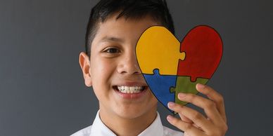 A boy smiles holding a heart-shaped puzzle piece with colorful segments.