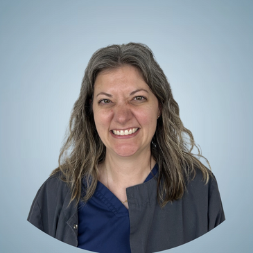 Smiling woman with gray hair in a dark jacket and blue shirt against a light blue background.