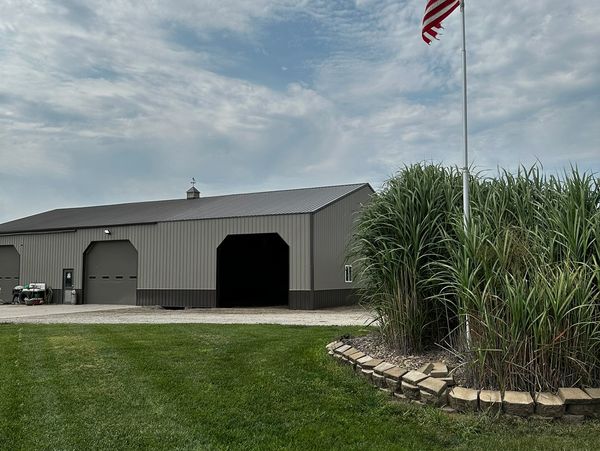American flag flying beside a large gray barn under a cloudy sky.