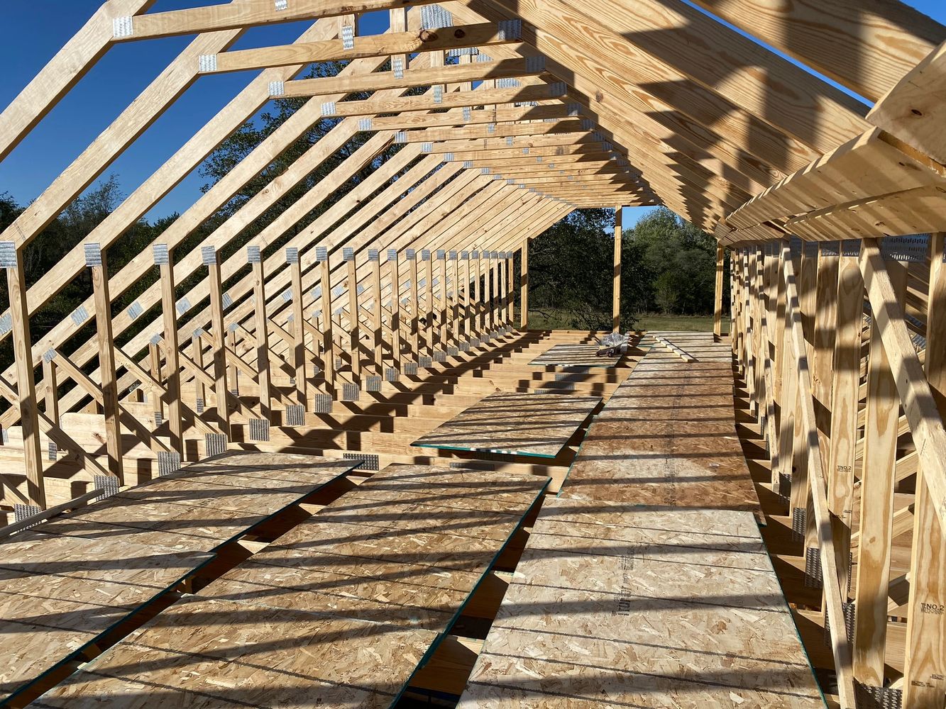 Wooden frame structure of a building under construction with sunlight casting shadows.
