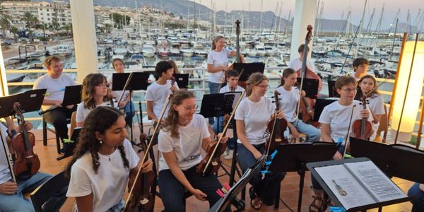 Young musicians in white shirts playing string instruments by the marina.