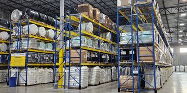Organized warehouse with stacked pallets and rolls on blue and yellow metal racks.
