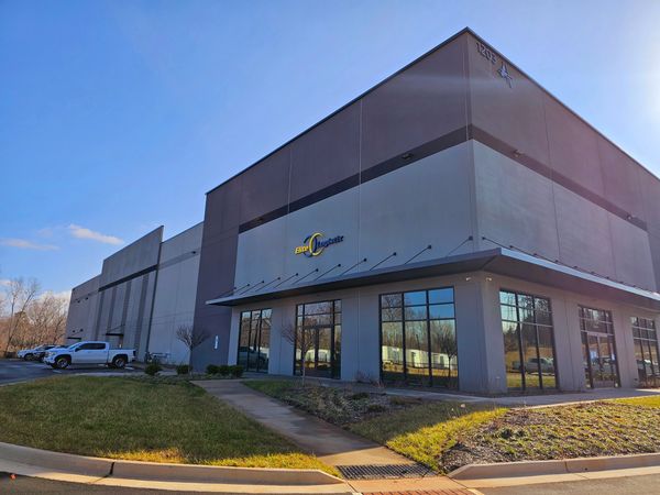 Modern commercial building with Elite Logistics sign and parked vehicles under clear blue sky.