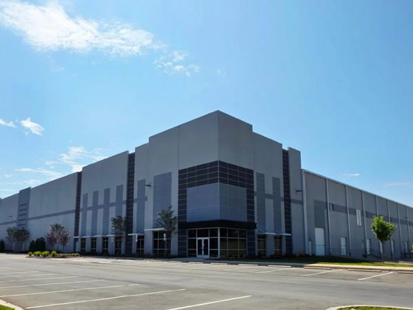 Modern industrial warehouse with clear blue sky and empty parking lot.